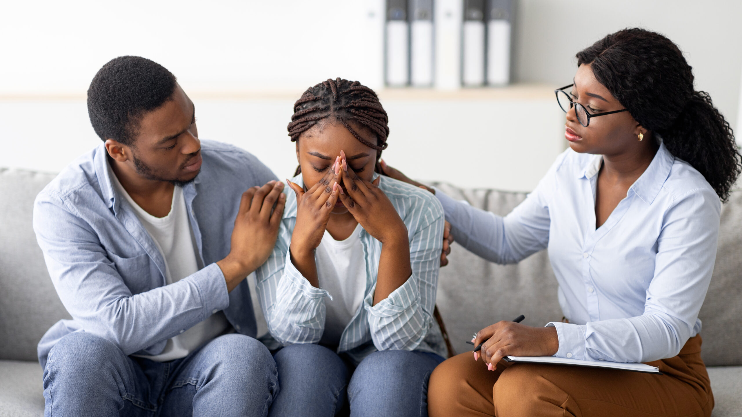 Empowerment After Domestic Assault young black woman crying at therapist's office, affectionate husband supporting her with professional psychologist